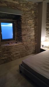 a bedroom with a stone wall with a bed and a window at Aegean Deep Blue Andros Ano Aprovato in Apróvaton
