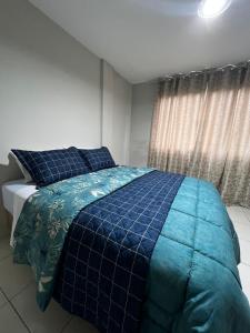 a bedroom with a bed with a blue comforter and a window at Hotel APART Zuccolotto 303 in Aracruz