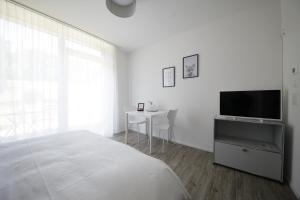 a white bedroom with a bed and a tv and a table at VARIAS Lifestyle Apartments in Elsau