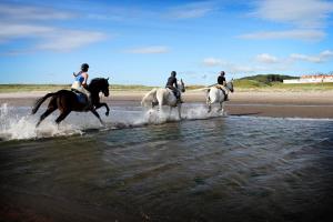 três pessoas andando a cavalo na água na praia em Trump Turnberry em Turnberry