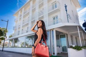 a woman standing in front of a building with a red bag at Hb Hotels Orchidea Blu in Rimini
