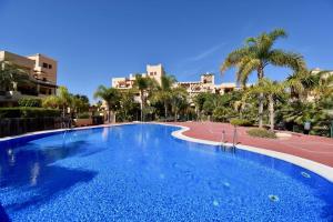 une grande piscine bleue avec des palmiers et des bâtiments dans l'établissement Marinas Sunset - Tu Dúplex con Solarium Privado!, à Vera