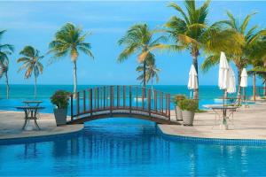 a bridge over a pool with palm trees and the ocean at WaiWai Cumbuco #406 - Apê na Praia por Carpediem in Cumbuco