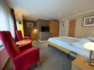 a bedroom with a bed and two chairs and a television at Landhotel Alberts in Heijenrath