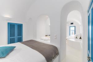 Dormitorio blanco con cama y puerta azul en Aristos Life Luxury Cave Villas, en Oia