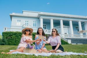 three women sitting on a blanket in front of a white house at Hotel Haikko Manor & Spa in Porvoo