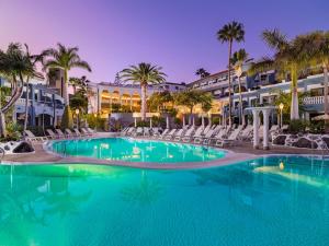 uma grande piscina com cadeiras e palmeiras em frente a um hotel em Adrián Hoteles Colón Guanahaní Adultos Only em Adeje