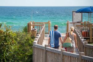 a man and woman walking down a wooden walkway to the beach at WaterColor Inn & Resort in Santa Rosa Beach