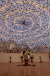 a woman sitting in a yoga position in a room with a large ceiling at Baja Nomads Hotel - Adults 15 Plus in Todos Santos