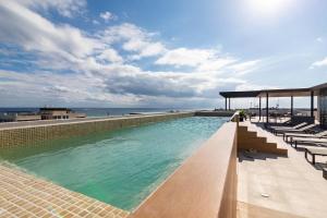 a swimming pool with chairs and the ocean in the background at 2BR Modern 5th Avenue Apt -Distrito Corazon D1 in Playa del Carmen