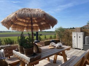 una mesa de madera con una sombrilla de paja en una terraza en Cabin De Duinweg: direct aan duin en bos, en Noordwijk