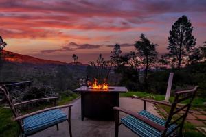 a fire pit on a patio with two chairs and a sunset at Sierra Vista Lookout Lodge with Creek, Waterfall and Waterholes, minutes from Bass Lake and Yosemite South Gate in North Fork