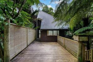 einen Holzsteg, der zu einem Haus mit einem Zaun führt in der Unterkunft A 1BR slice of Titirangi Heaven - WiFi - Netflix in Auckland
