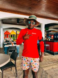 Um homem de camisa vermelha, óculos e chapéu. em THE BOARDWALK VILLAGE em Negril