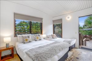 two beds in a room with two windows at Fuller Holidays - Belongil Beachfront Pavilion, 18 Childe St in Byron Bay