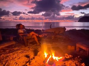 a woman sitting around a fire on the beach with a dog at Camp Tarimbang in Tandulujangga