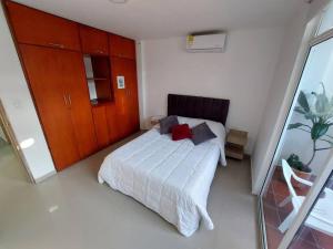 1 dormitorio con cama blanca y almohadas rojas en Hermoso Apartamento Cerca a la Playa Puerto Colombia, en Puerto Colombia