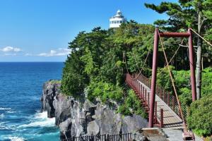 un ponte sospeso con un faro in cima a una scogliera di ファスティングホテル海の杜 a Kannami