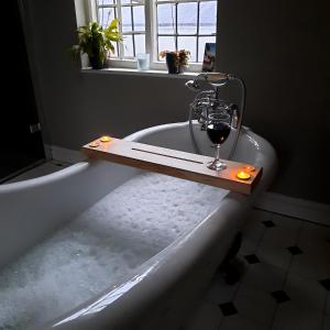 Wilde Rooms في Weston: حوض استحمام مع كوب من النبيذ يجلس عليه
