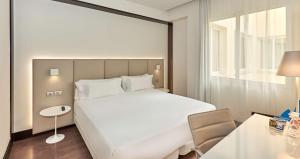 a bedroom with a large white bed and a table at NH Madrid Lagasca in Madrid