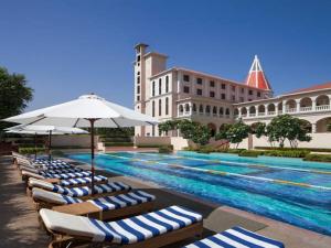 a pool with lounge chairs and umbrellas next to a building at DLF Club 5 in Gurgaon