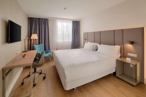 ブラニャックにあるNH Toulouse Airportの大きなベッドとデスクが備わるホテルルームです。