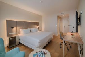 a hotel room with a large white bed and a desk at NH Toulouse Airport in Blagnac