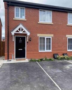 un edificio de ladrillo con una puerta negra en un estacionamiento en Fresh & Spacious New Build Home, en Church Coppenhall