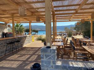 eine Terrasse mit Holztischen und -stühlen und einem Strand in der Unterkunft Helios Beach Hotel & Bungalows in Karpathos