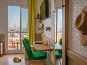 a room with a desk and green chairs and a balcony at ibis budget Menton Bord de Mer in Menton