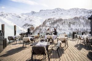 um restaurante com mesas e cadeiras num deque com montanhas cobertas de neve em Bergman Mountain Hotel em Breuil-Cervinia