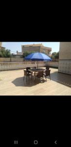 a table with a blue umbrella and two benches at Bol d'air à la mer centre Ain el Turck in Aïn El Turk