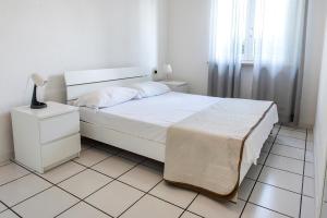een witte slaapkamer met een bed en een lamp op een tegelvloer bij N169 - Numana, nuova villa quadrilocale con giardino in Numana