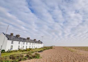 a white house on the beach with a gravel road at 6 Coastguard Cottages in Hollesley