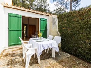 a white table and chairs on a patio with green doors at Holiday Home Bois d'Eleis-2 by Interhome in La Palmyre