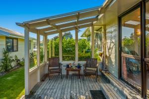 porche cubierto con 2 sillas y mesa en Waikanae Waves - Waikanae Beach Holiday Home, en Waikanae