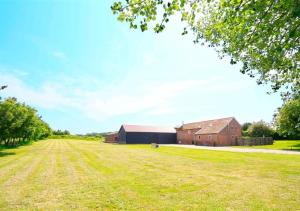an empty field next to a barn and a building at East Barn Cottage in Aldringham