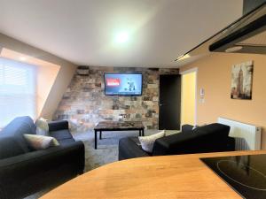 een woonkamer met banken en een tv aan een bakstenen muur bij New County Hotel & Serviced Apartments by RoomsBooked in Gloucester