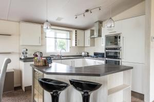 una cocina con armarios blancos y taburetes negros en Bude Holiday Resort, en Bude