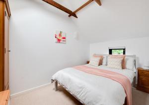 ein weißes Schlafzimmer mit einem Bett mit orangefarbenen und weißen Kissen in der Unterkunft Lake Farm Barn in Holbrook