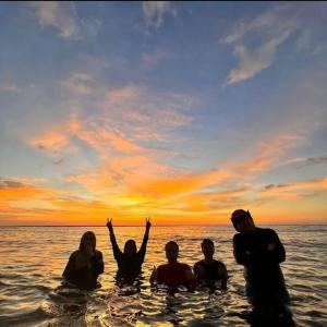 een groep mensen die bij zonsondergang in het water staan bij Private Beach House with Sunset View @ Kuala Penyu Sabah in Kampong Tidong