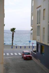 a red car parked on a street next to the ocean at Apartamento El Sol Naciente in La Herradura