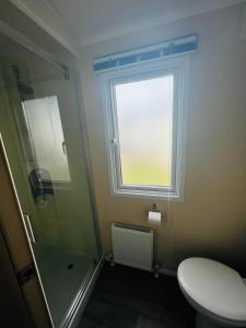 a bathroom with a shower and a toilet and a window at Lets Host Hot Tub Holiday Home with Lake view in Patrington