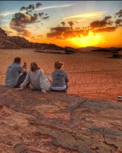 three people sitting on the beach watching the sunset at Enad desert camp in Wadi Rum