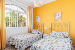 two beds in a bedroom with yellow walls and a window at Chalet Fuente1 piscina común famila in Conil de la Frontera +8 photos