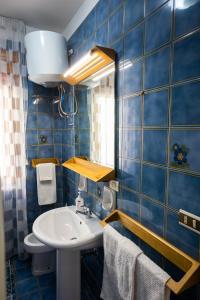 La salle de bains est pourvue de carrelage bleu, d'un lavabo et d'un miroir. dans l'établissement Gilda’s Home, à Scalea