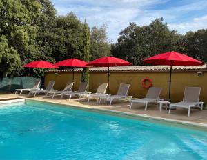 a pool with chairs and red umbrellas next to it at Logis La Bastide De Grignan Hotel & Restaurant "La Chênaie" in Grignan