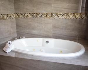 a white tub in a bathroom with a tile wall at Golden Bay Belize Hotel in Belize City