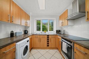 cocina con armarios de madera, lavadora y secadora en Three Bedroom Home Near Central Milton Keynes by HP Accommodation with Free Parking, WiFi & Sky TV, en Milton Keynes