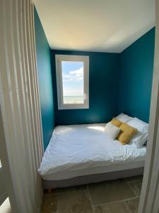 Cette chambre bleue comprend un lit et une fenêtre. dans l'établissement Appartement vue sur l'océan, à La Parée Preneau